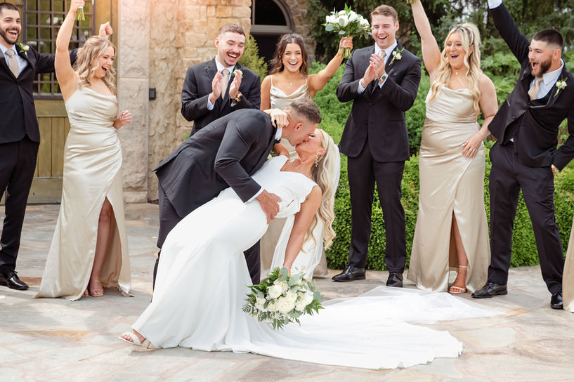 Groom dips his bride for a kiss while wedding party cheers in front of integrity hills in Branson 