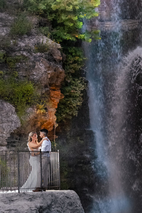 Newly married couple kisses on a bluff at nighttime with a waterfall at Dogwood Canyon in the Background