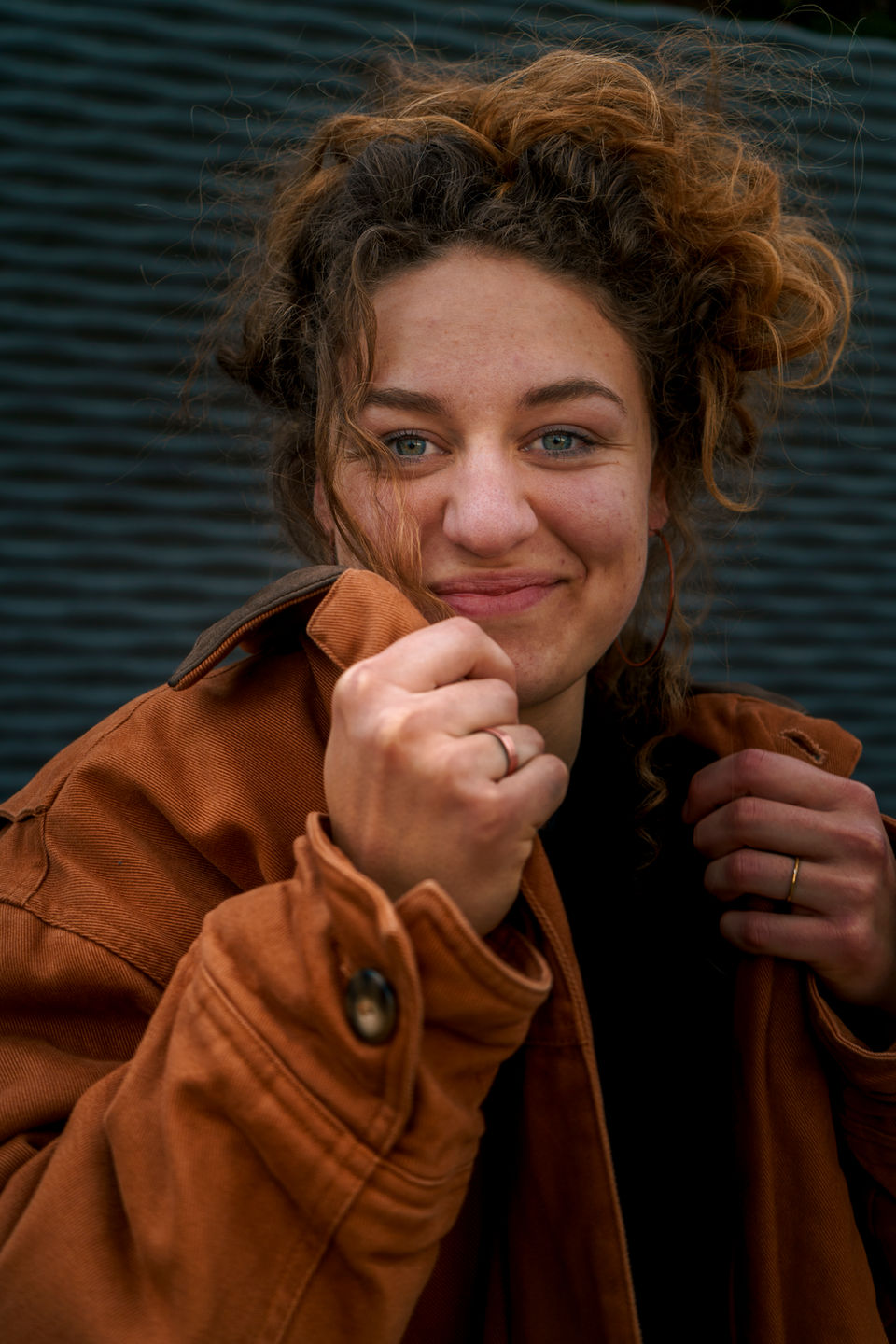 junge Frau lächelt in die Kamera, während sie ihre Jacke berichtigt.