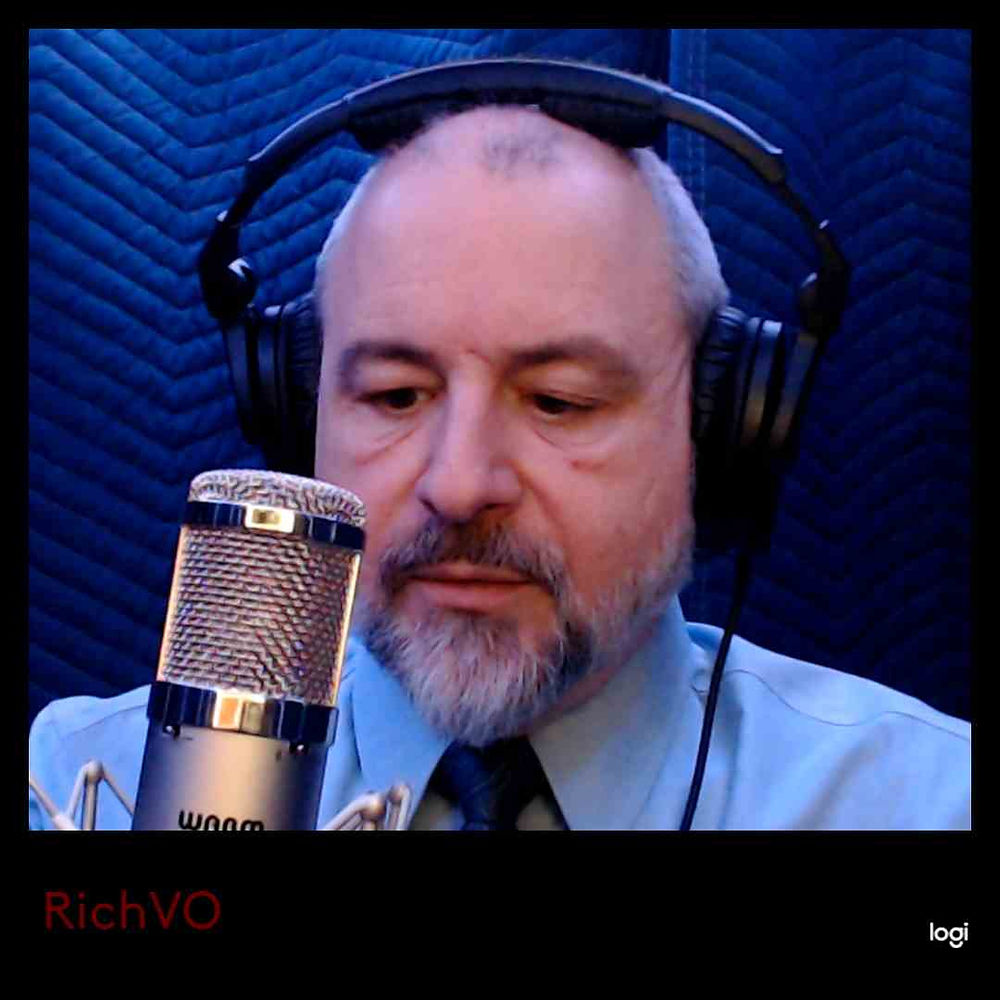Rich in shirt and tie behind a mic looking down reading script