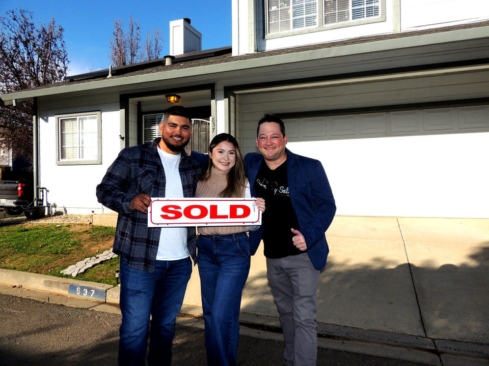 Hector and Jennifer, first-time homebuyers, celebrating with their Realtor Scott Sweeney in front of their new home in Galt, CA, holding a sold sign.
