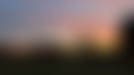 A sunset with a silhouette of a home and trees in the distance.