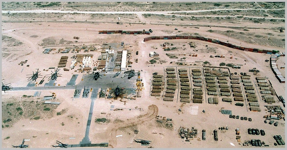 High-angle aerial view of a U.S. military base situated in a desert landscape, featuring orderly rows of tents, tactical vehicles, and several damaged military helicopters stationed on the tarmac.