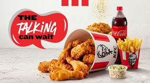 KFC meal with fried chicken spilling from a bucket, fries, coleslaw and Coca-Cola beside The talking can wait slogan on red backdrop, fast food marketing at its finest: a tempting display of fried chicken, fries, coleslaw, and a soft drink showcases how the industry captures consumer cravings.