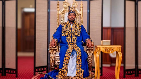 King Oyo Nyimba Kabamba Iguru Rukidi IV of Tooro Kingdom is seated on his ornate golden royal throne, wearing royal blue and gold embroidered ceremonial robes with his feet resting on a leopard skin.