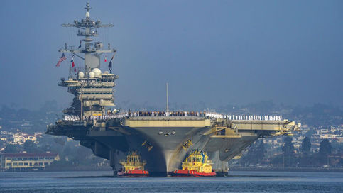 The U.S. Navy aircraft carrier USS Abraham Lincoln (CVN 72) towed by tugboats with sailors standing on the flight deck, amid news reports regarding Iranian missile claims and crew deployment strain.
