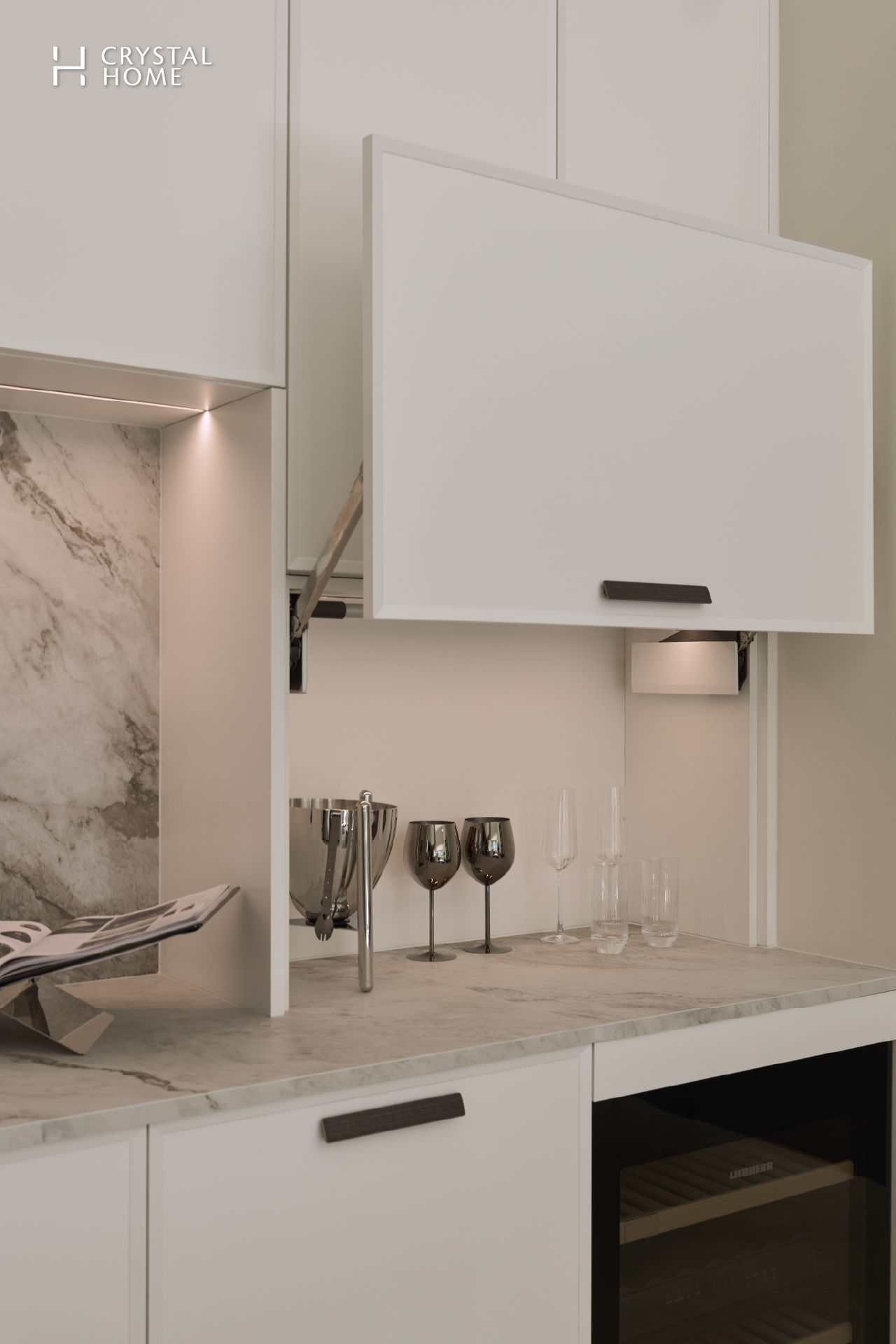 Contemporary Italian kitchen cabinet system from Composit featuring a lift-up wall unit, marble backsplash, and elegant glassware styling on a clean, minimalist countertop.