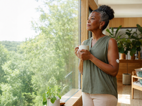 Elegant midlife woman with a continuous glucose monitor thoughtfully looking out a bright window, representing a mindful approach to diabetes safety and holistic self-care.