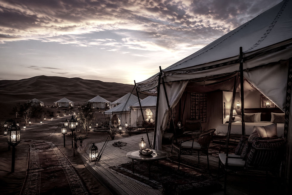 Campamento de lujo en el desierto de Marruecos al atardecer, con tiendas privadas y dunas de arena roja