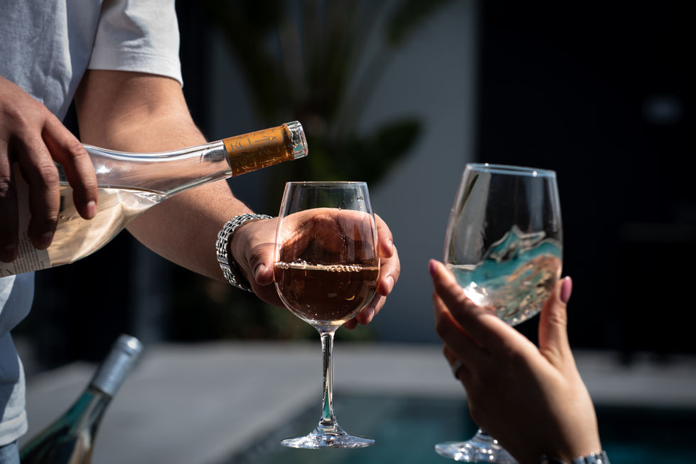 מזיגת יין לבן אל תוך כוסות קיץ עם נוף בריכה