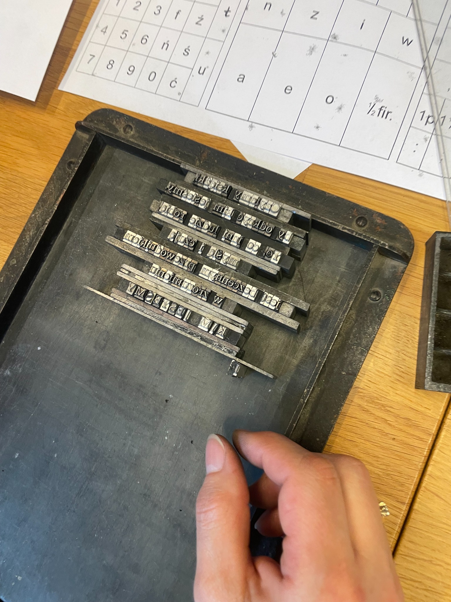 Metalowe czcionki ułożone w formie typograficznej i dłoń przy ręcznym składzie.