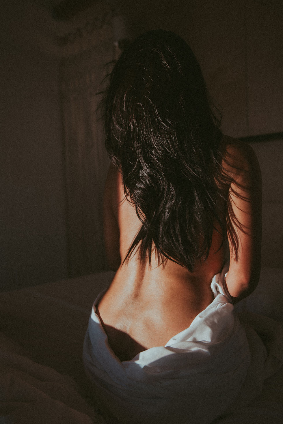 Woman sitting on bed, back view with sunlight, Fine Art, artistic photo.