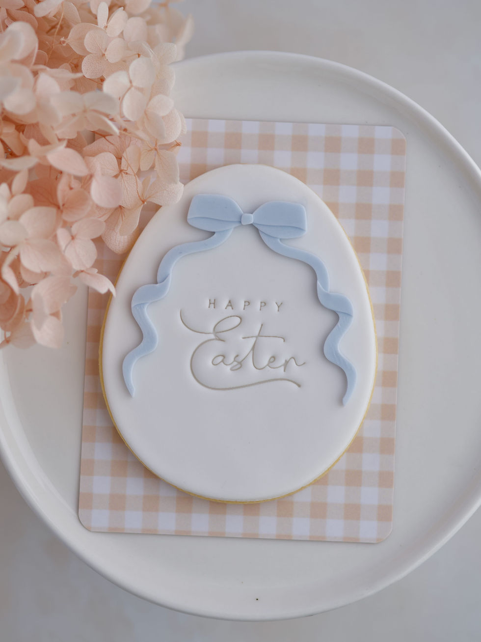 White fondant Easter egg cookie with blue bow and “Happy Easter” stamp.