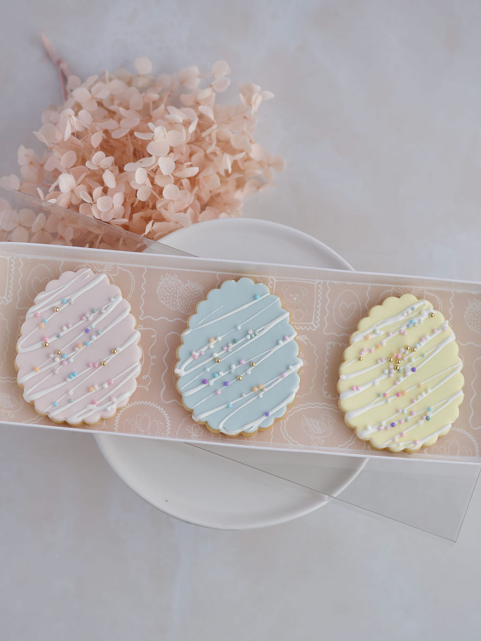 Three pastel Easter egg sugar cookies with white drizzle and sprinkles in gift box.