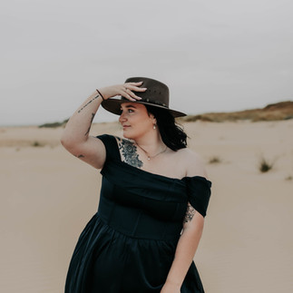 Woman in blue off the shoulder dress with hand on hat on the beach on an overcast day