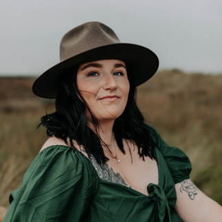 Woman in brown hat and green dress sitting with grass in the background