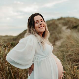 Pregnant woman in white dress holding belly in a grassy landscape