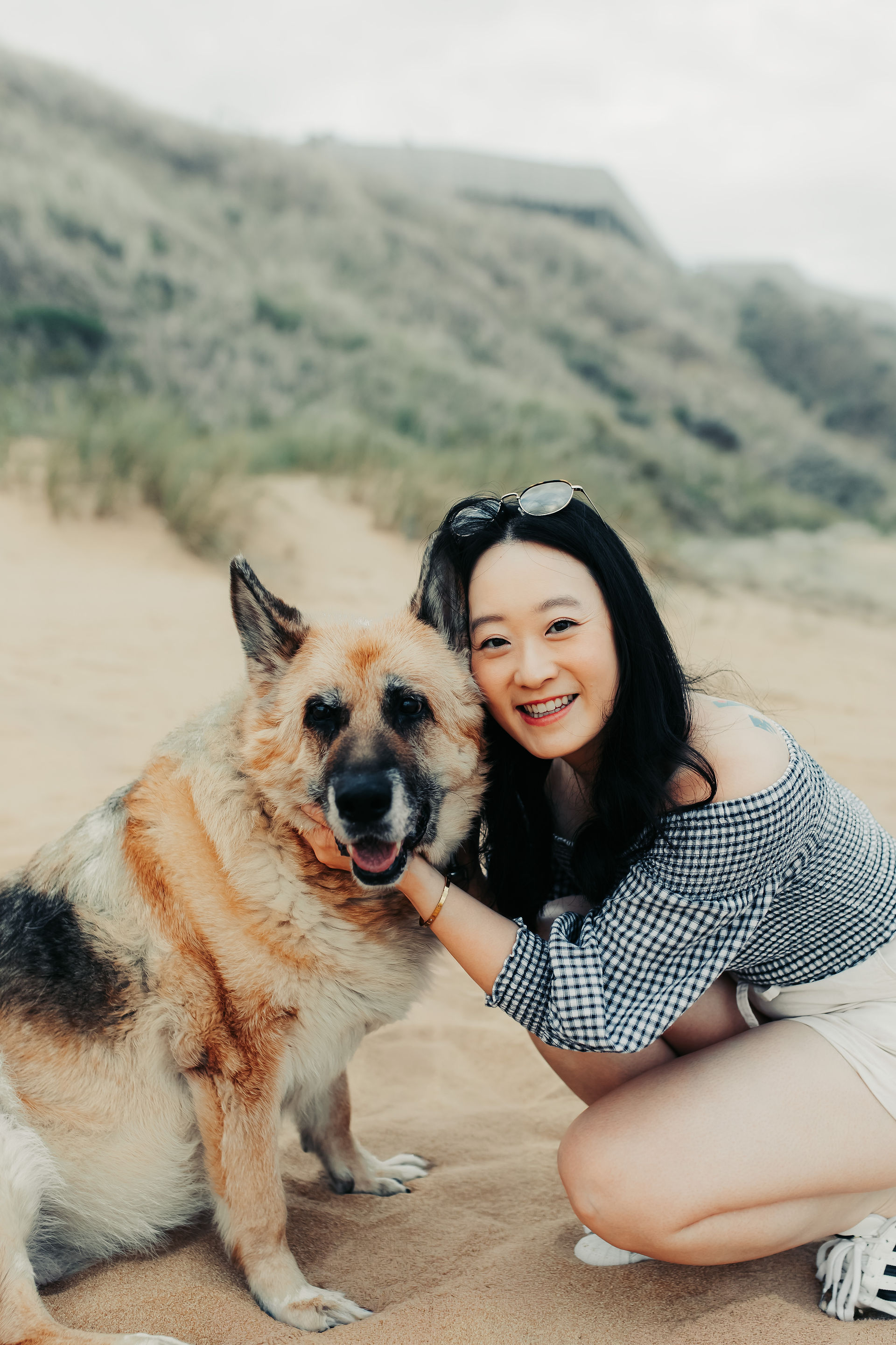 Woman hugs German Shepard on a beach with salt bushes in the background
