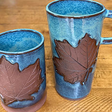 2 green mugs with a maple leaf decoration sitting on a wooden table