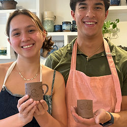 a woman and a man wearing aprons holding hand built unglazed espresso cups