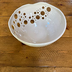 White handmade fruit bowl with round holes at the top on a wooden table