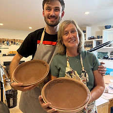 a mother and son wearing aprons holding clay bowls