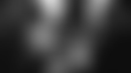 Person in bar holding phone displaying their bar loyalty app, bartender in white shirt smiling nearby. Dimly lit, lively atmosphere. Black and white.