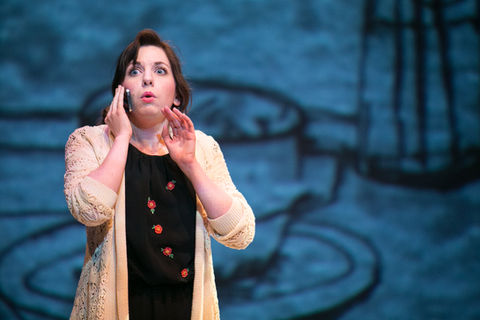 A woman holds a cell phone to her ear and looks upward with concern under blue stage lighting - Dead Man's Cell Phone