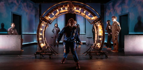 A performer stands before a large illuminated circular portal on stage - The Light Chasers