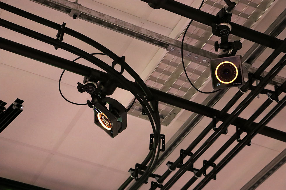 Ceiling-mounted black OptiTrack cameras and rails in an indoor studio, with glowing orange rings and a small blue 14 display.