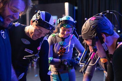 mocap actors in suits and head rigs smiling looking at a script