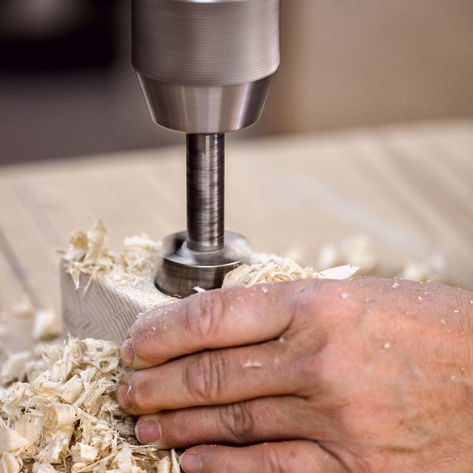 Ein Handwerker bohrt ein Loch in ein Stück Holz bei der Lebensarbeit Werkstatt in Salzburg.