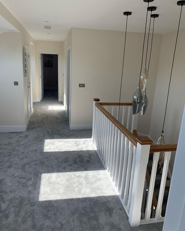Hallway with gray carpet, white banister, and hanging lights. Mr H Carpets & Flooring.