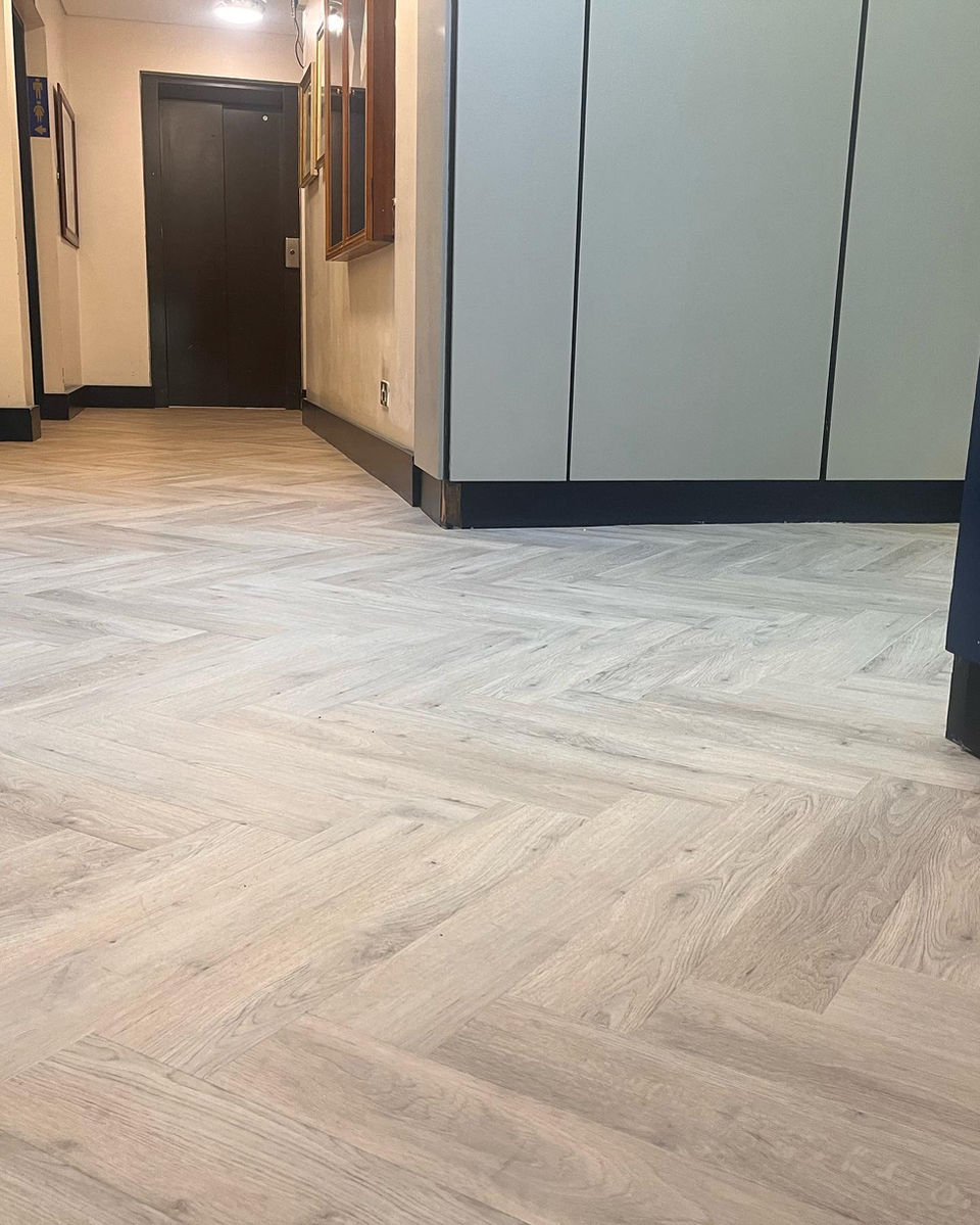 Herringbone hardwood flooring, entryway, dark door, neutral walls, and trim.