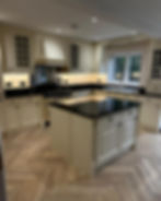 Elegant kitchen with cream cabinets and black countertops, with hard wood flooring.