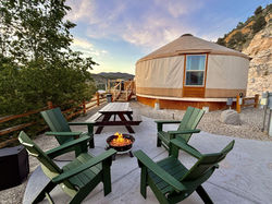 Green camp chairs, firepit, and picnic table on the patio of a yurt.