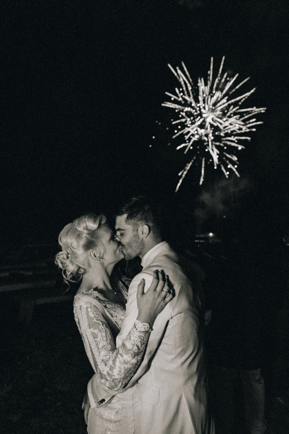A bride and groom kissing while fireworks are going off in the background.