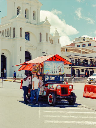 Analog photo of a red coffee-selling jeep parked in front of a white church in Marinilla, Colombia, with people gathered around.