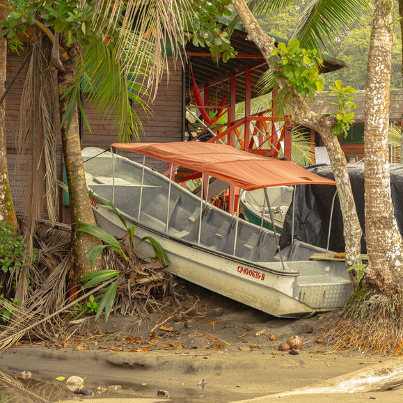 Photo of a fiberglass boat with an orange canopy on the shore in Nuquí, Colombia, surrounded by palm trees and wooden structures.