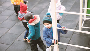 5 small children wrapped up for cold weather, playing in a play area.