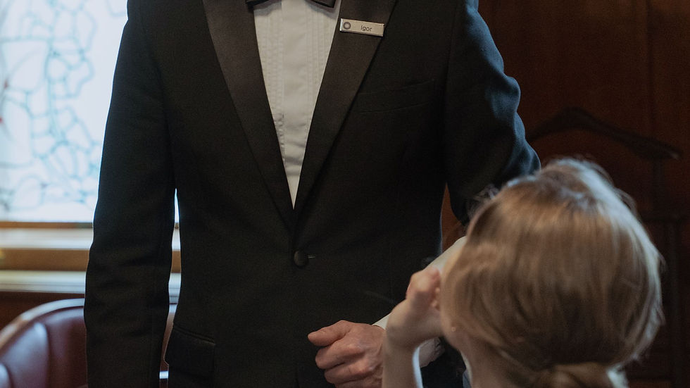 A suited waiter speaking with a seated restaurant guest