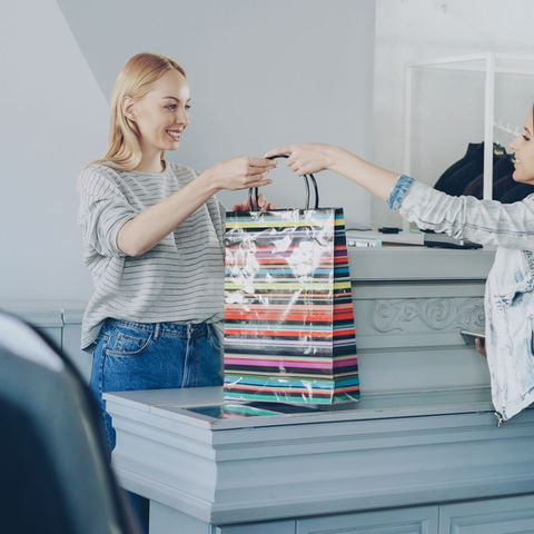 Retail colleague handing a shopping bag to a customer; illustrative stock photograph