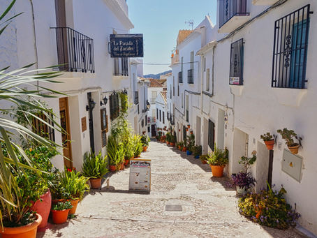 Narrow cobblestone street in Frigiliana, Spain,  lined with white buildings, potted plants, and a sign reading "La Parada del Zacalín." Bright, sunny setting.