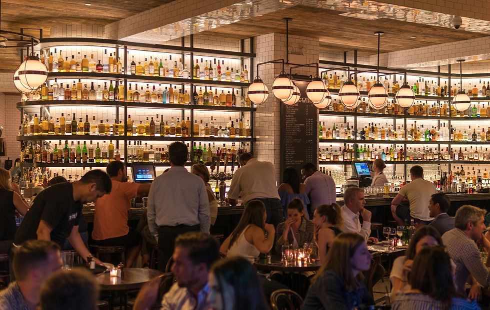 Bustling bar in the Algarve with people socializing, surrounded by shelves filled with bottles. Warm lighting creates an inviting atmosphere.