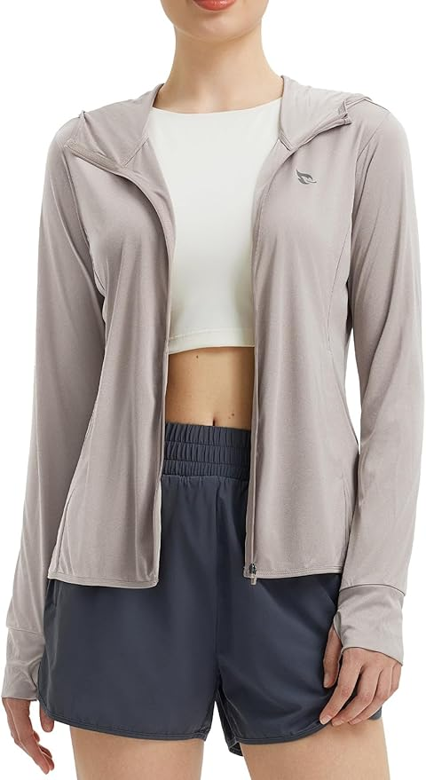 Woman wearing light gray BAleaf, UPF 50+ zip-up hoodie, white crop top, and dark shorts. Neutral expression, plain white background.