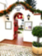 Entrance to "Fortaleza da Luz" restaurant with a red gate, orange flowers, and white walls. Text reads "1670" with warm lantern lights.