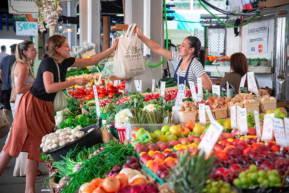 Woman buying produce at vibrant market, exchanging a bag with a vendor. Stalls filled with colorful fruits and vegetables, lively atmosphere.