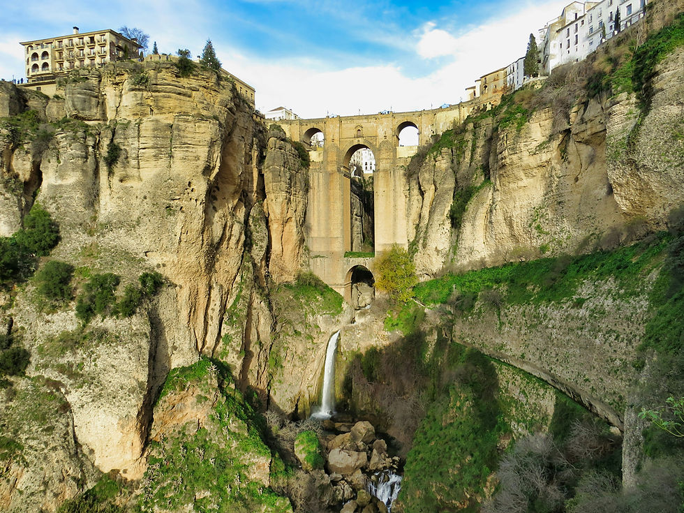 Ronda, Spain, Puente Nuevo. Stone bridge spans a deep gorge with a waterfall below in Ronda, Spain. Cliffs and buildings are visible under a bright blue sky.