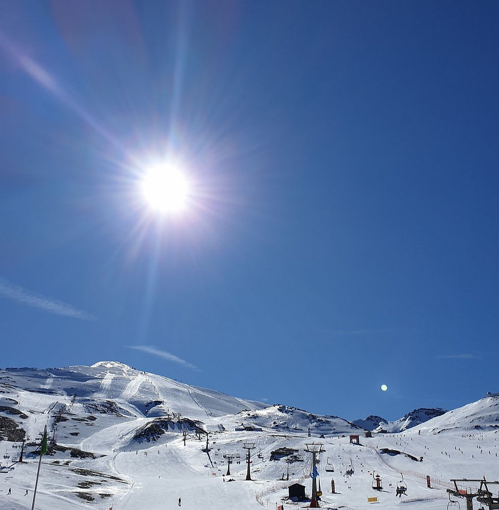 Sierra Nevada. Bright sun shines over a snowy mountain with skiers on the slopes. Clear blue sky and ski lifts in the foreground. Crisp, sunny winter day.