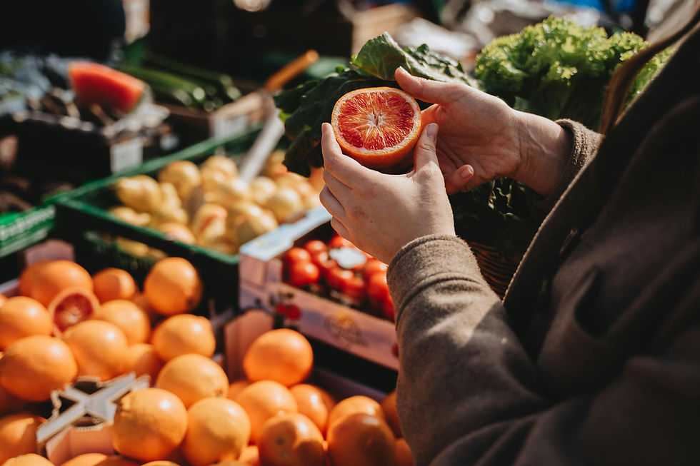 A market in the Algarve. Hands holding a halved blood orange over a market stall with fresh produce. Oranges and greens are visible, creating a vibrant scene.